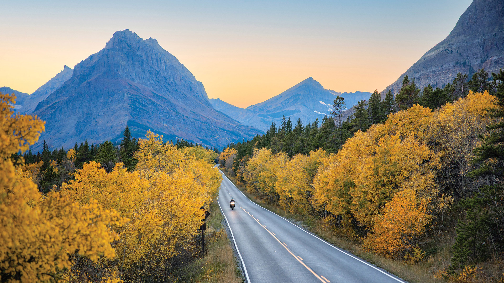 Driving a motorcycle through fall foliage and mountain scenery in Glacier National Park, Montana